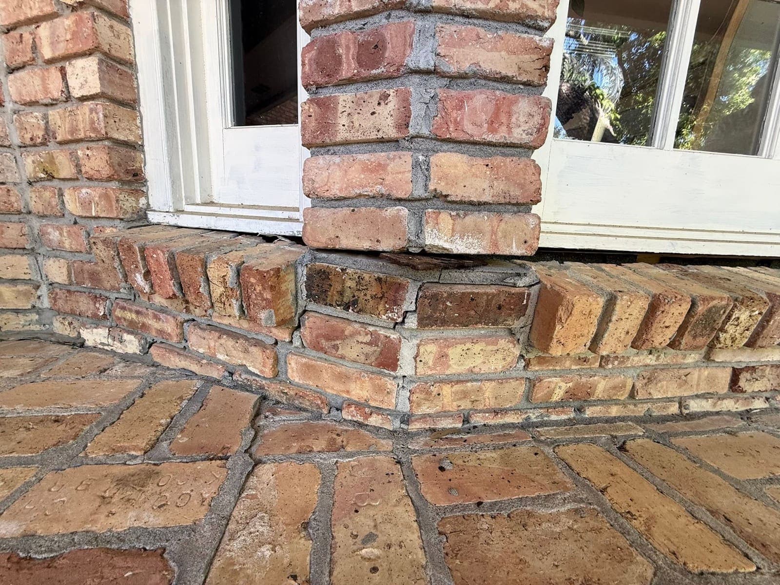 Cracked and settled stepped brick ledge running along the porch before repair