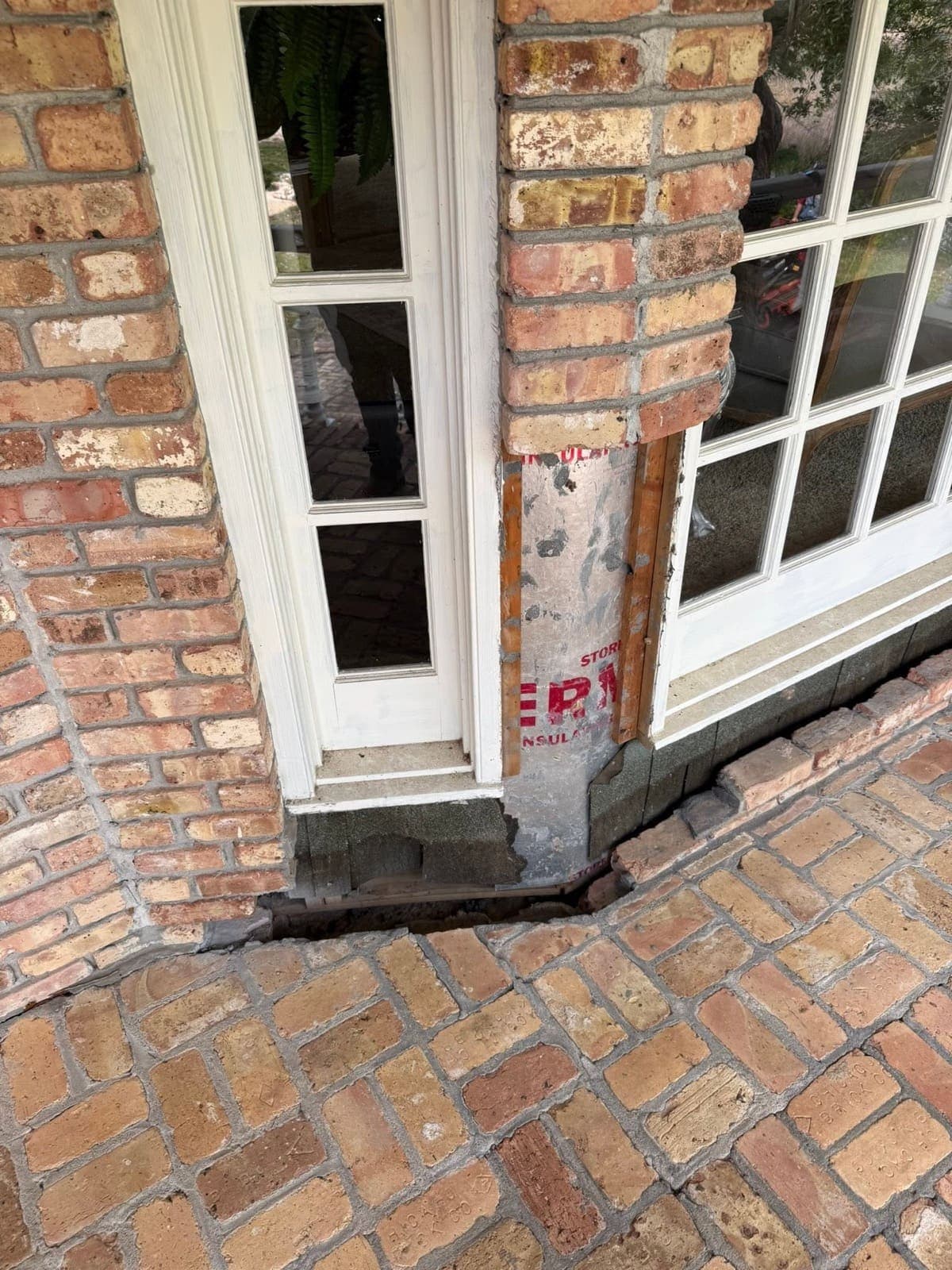 Large gap beneath the window where brick has dropped away, exposing sheathing and framing before the rebuild