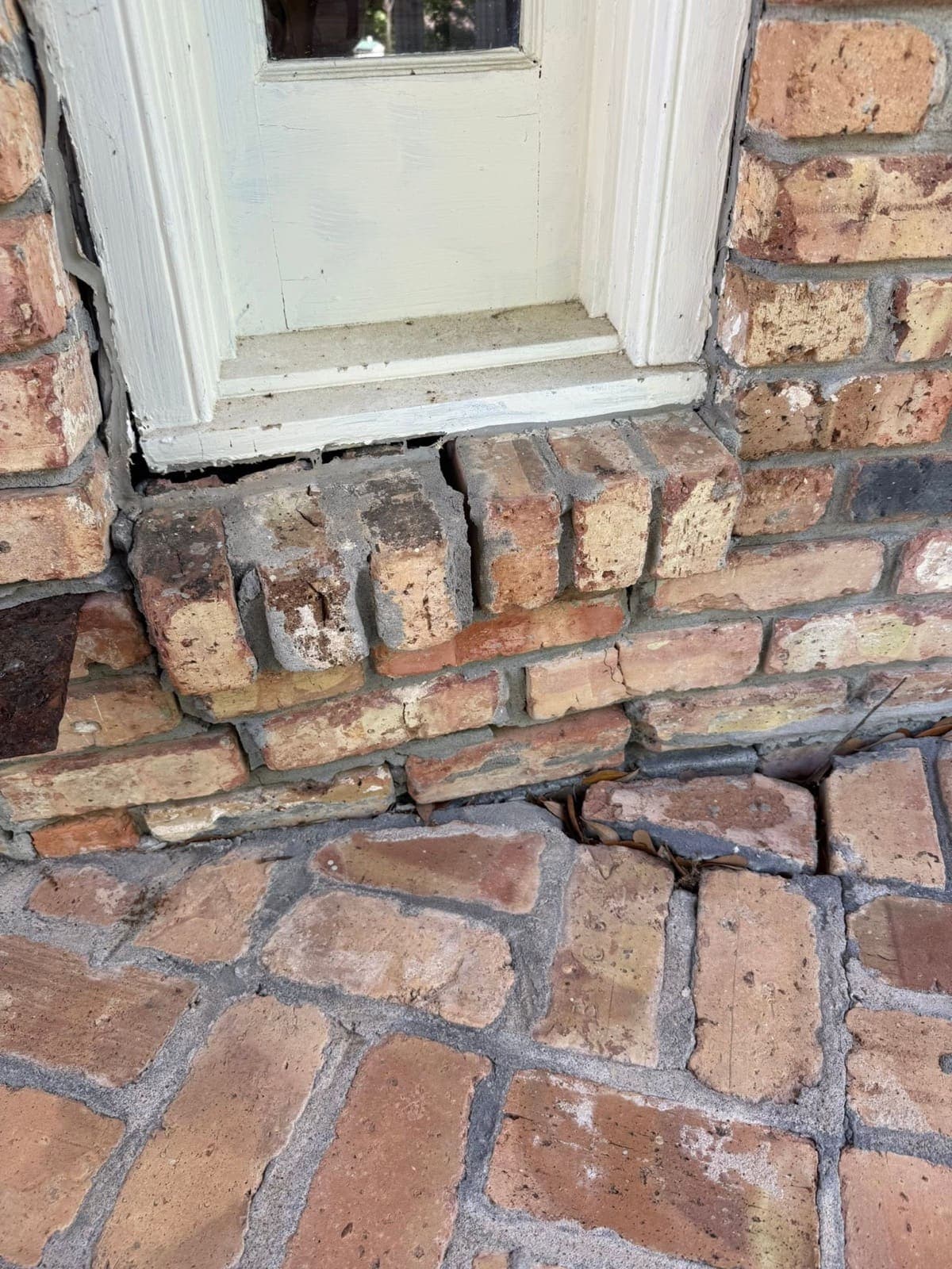 Cracked and displaced brick course under a window sill with an open gap into the wall