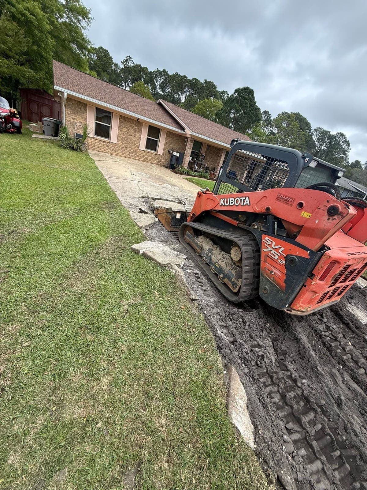 Compact track loader breaking out the cracked original driveway
