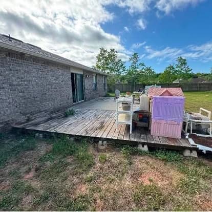 Weathered wood deck behind a brick home, boards greyed and sagging, before demolition