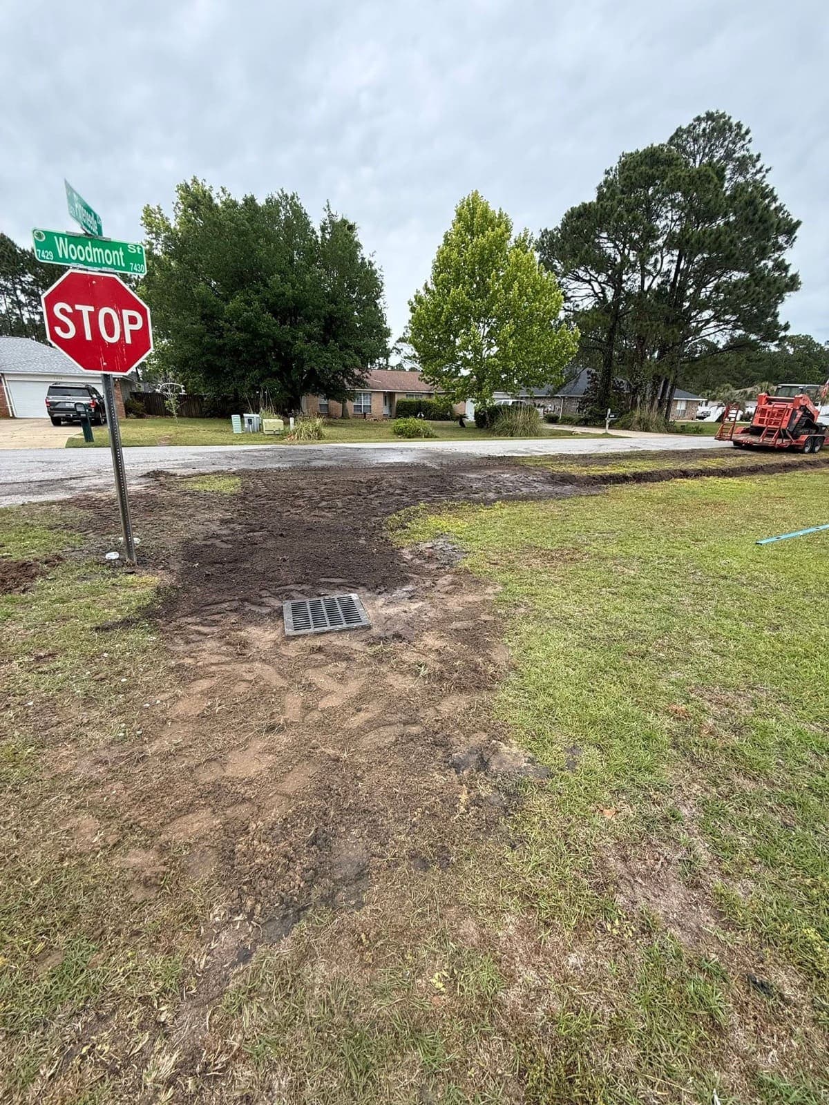Newly installed drain grate set flush in a regraded corner lot with fresh soil around it